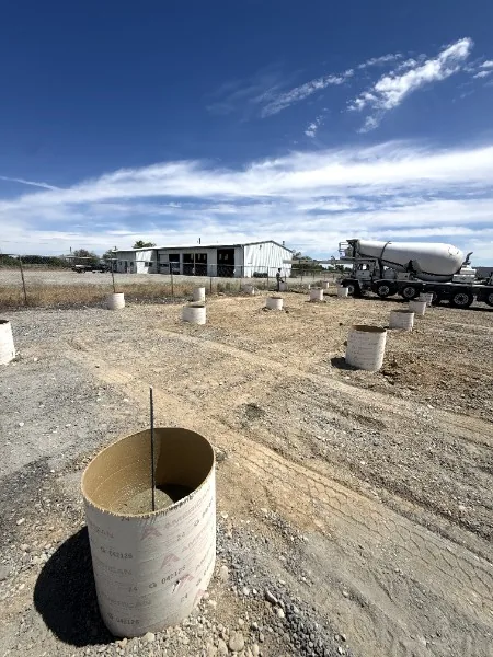 Concrete footing forms set on a gravel site with a mixer truck arriving