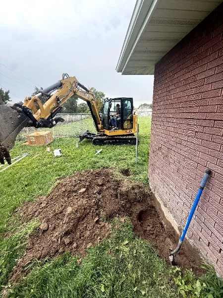 Excavator digging along a brick home's foundation