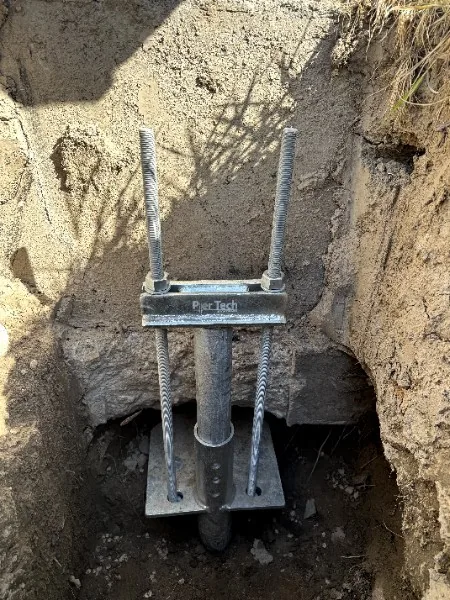 Helical pier bracket installed beneath a foundation footing