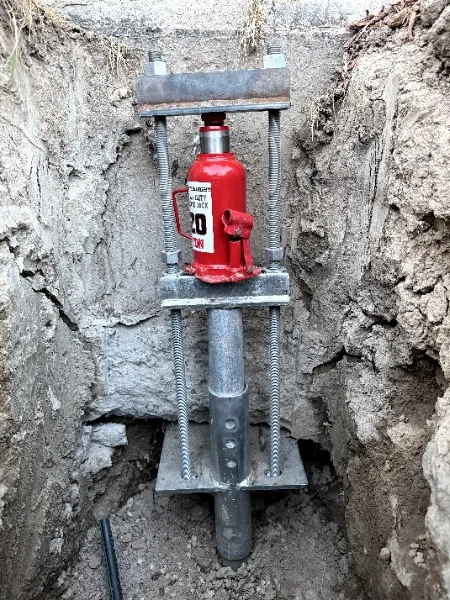 Hydraulic jack and bracket set on a foundation pier in an excavated hole