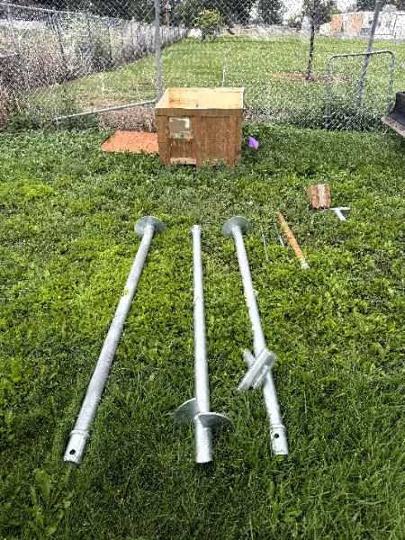 Three galvanized helical piers with screw-shaped plates laid out on the grass before installation