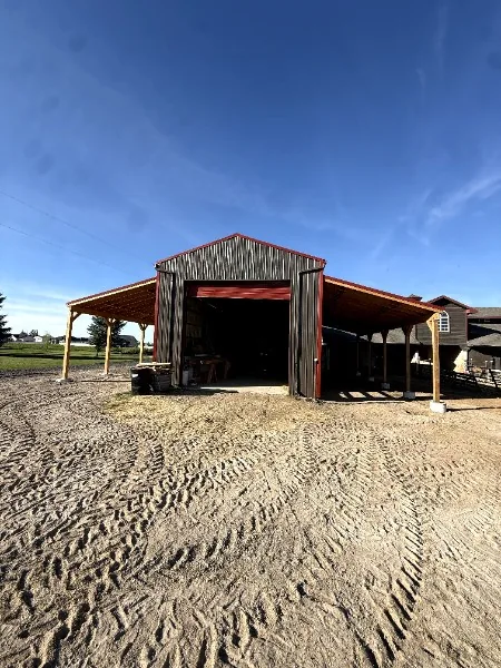 Finished pole barn with dark steel siding, red trim and timber-post lean-tos on both sides