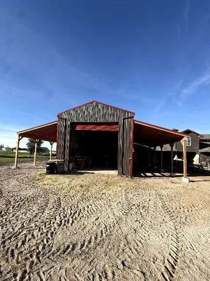 Finished pole barn with dark steel siding, red trim and timber-post lean-tos