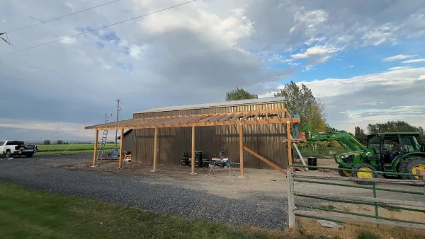 Timber pole structure framed in front of a steel building, with a tractor on site