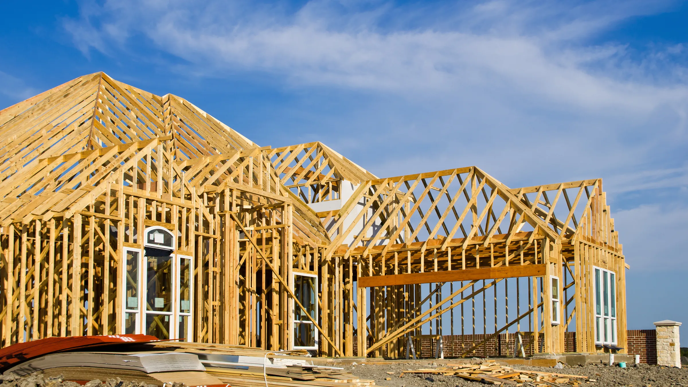 Wood-framed house under construction against a blue sky