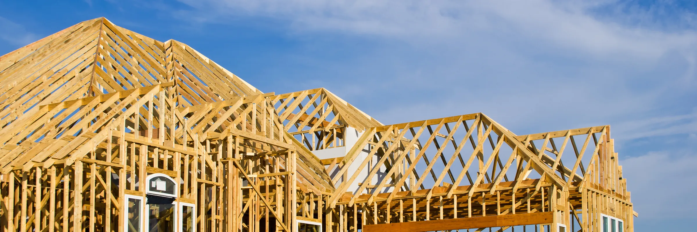 Wood-framed house under construction against a blue sky